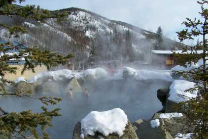 Snow-covered mountain hot spring with steam rising.